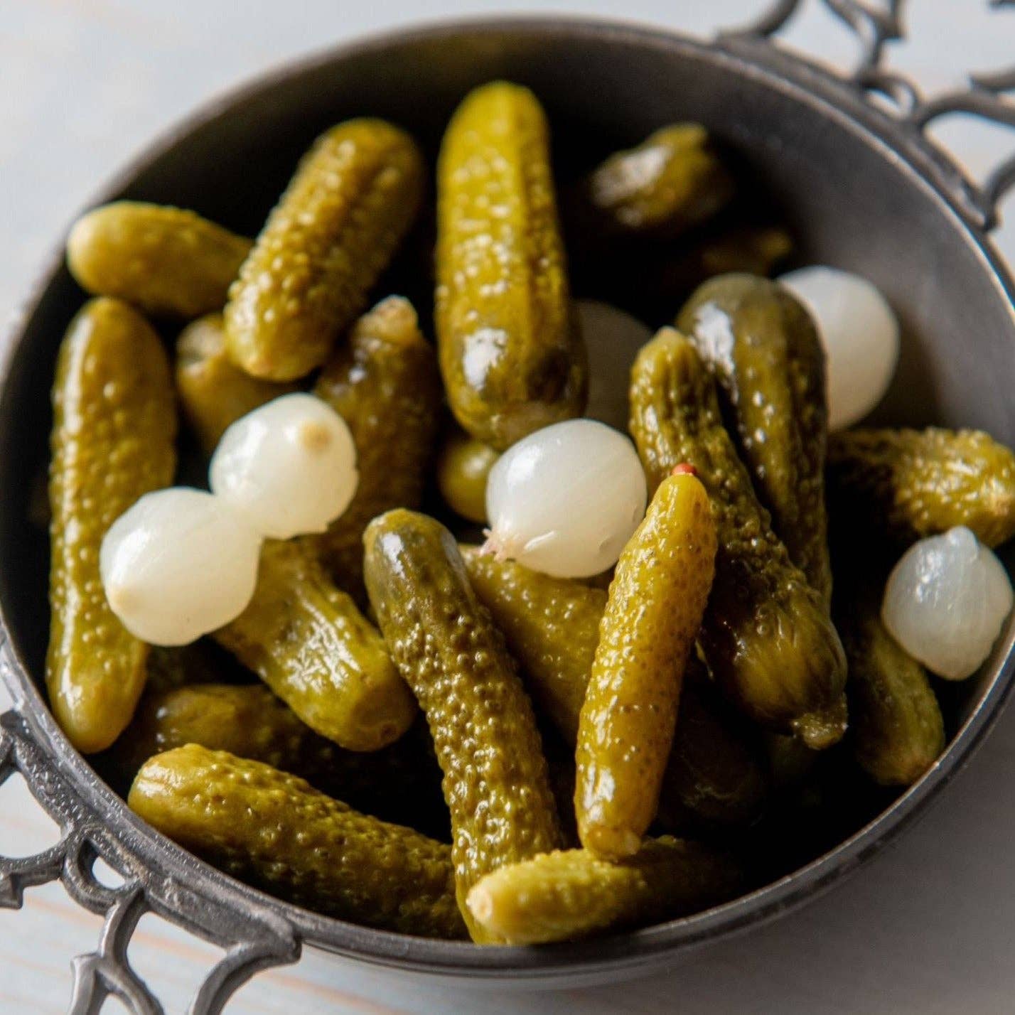 bowl of french cornichons and pearl onions on a white surface