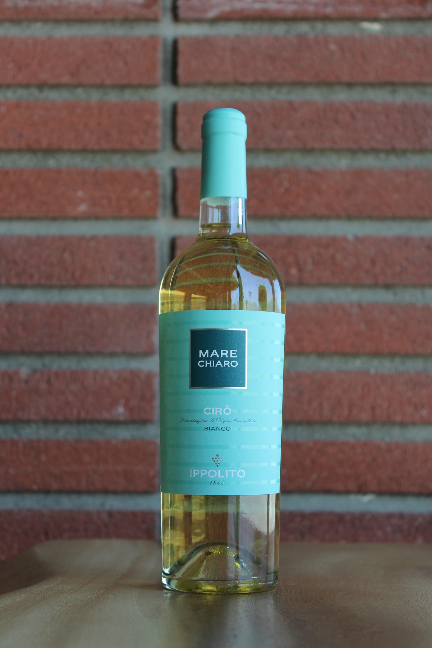 Bottle of Ippolito 1845 "Mare Chiaro" Greco Bianco on a wood surface with a red brick background