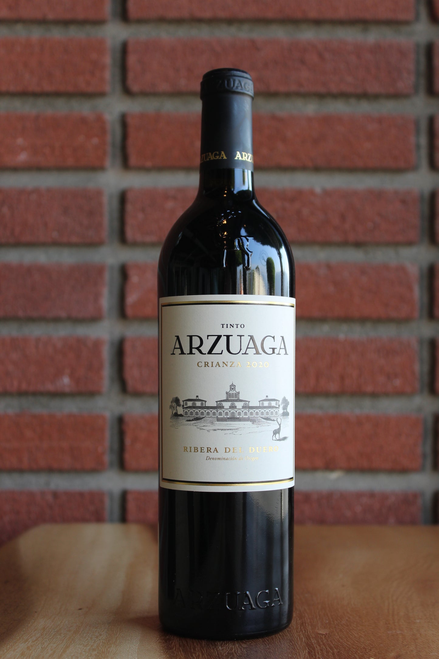 bottle of arzuaga crianza tempranillo on a wood table with a brick background