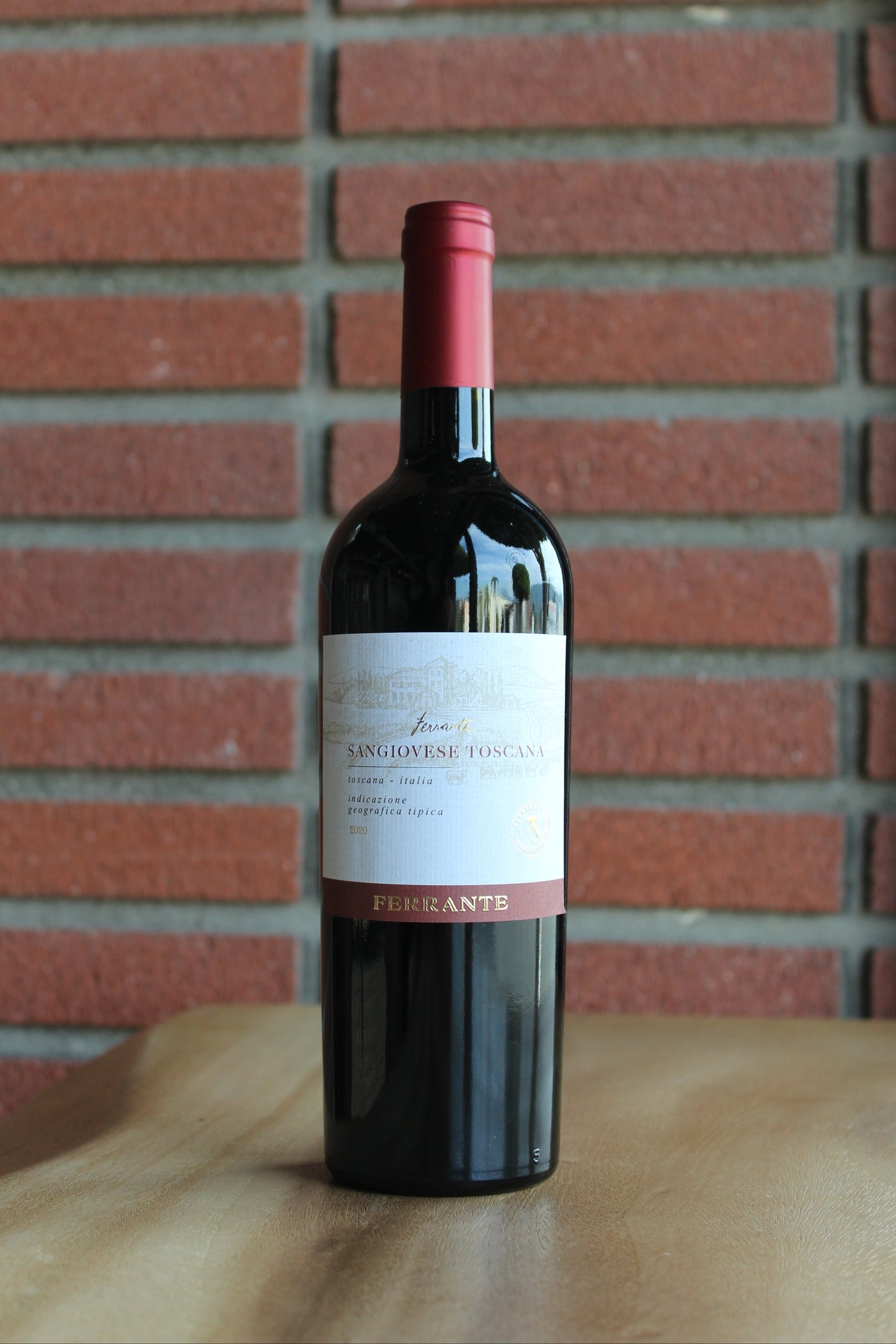 Bottle of Sangiovese Toscana Red Blend by Ferrante on a wood surface with a red brick background
