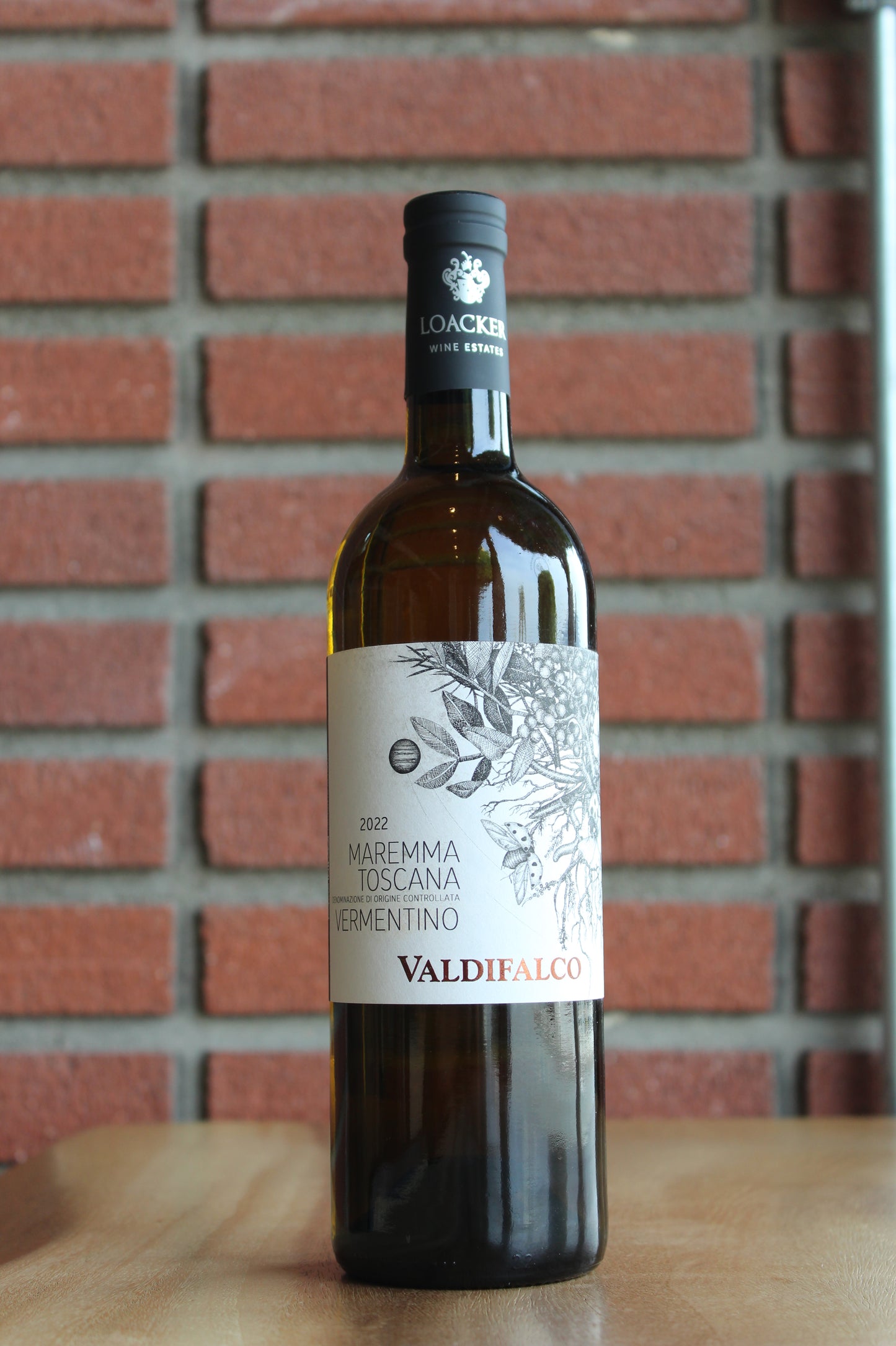 Wine bottle of Cascita Loacker Valdifalco Vermentino on a wood surface with a red brick background