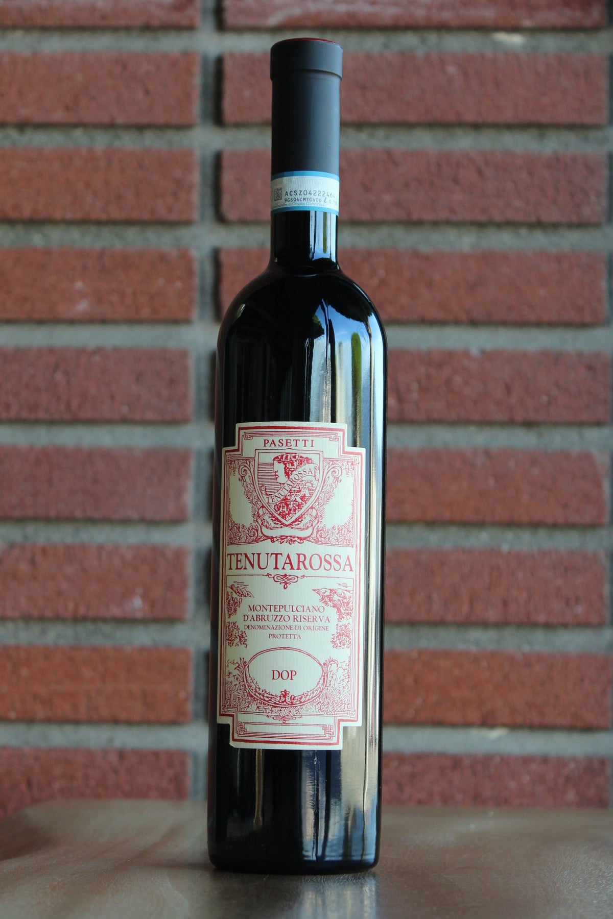 Bottle of Passetti Tenutarossa Montepulciano d'Abruzzo Riserva 2021 wine on a wood surface with a brick background