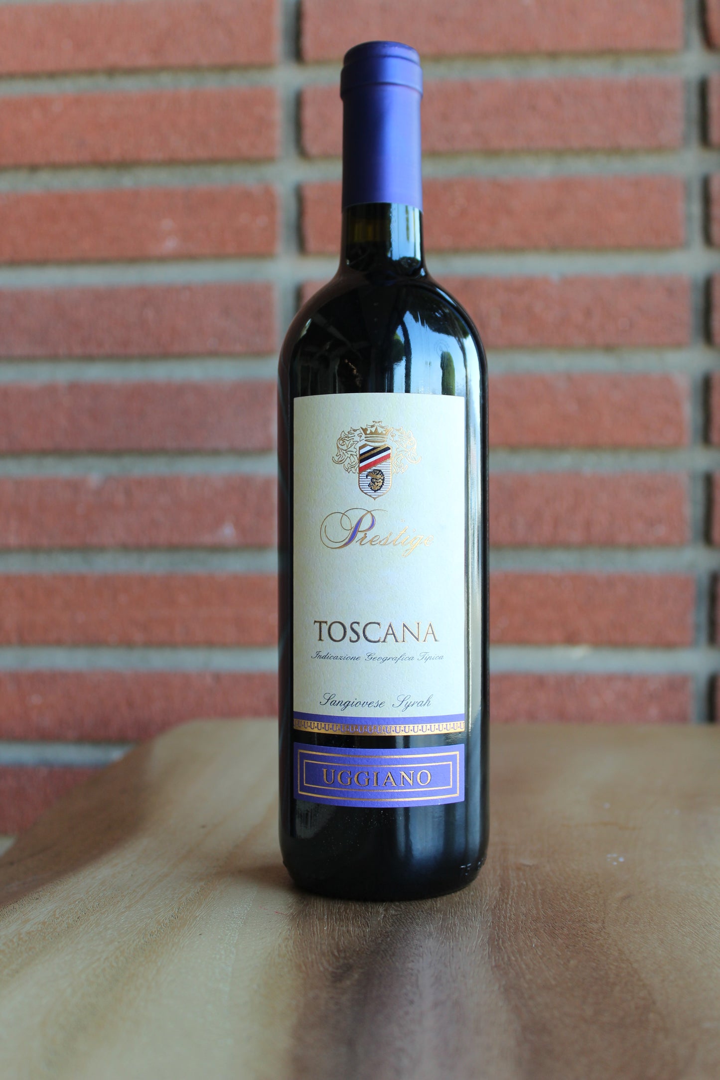 bottle of azienda uggiano prestige toscana sangiovese syrah red blend on wood table with red brick background