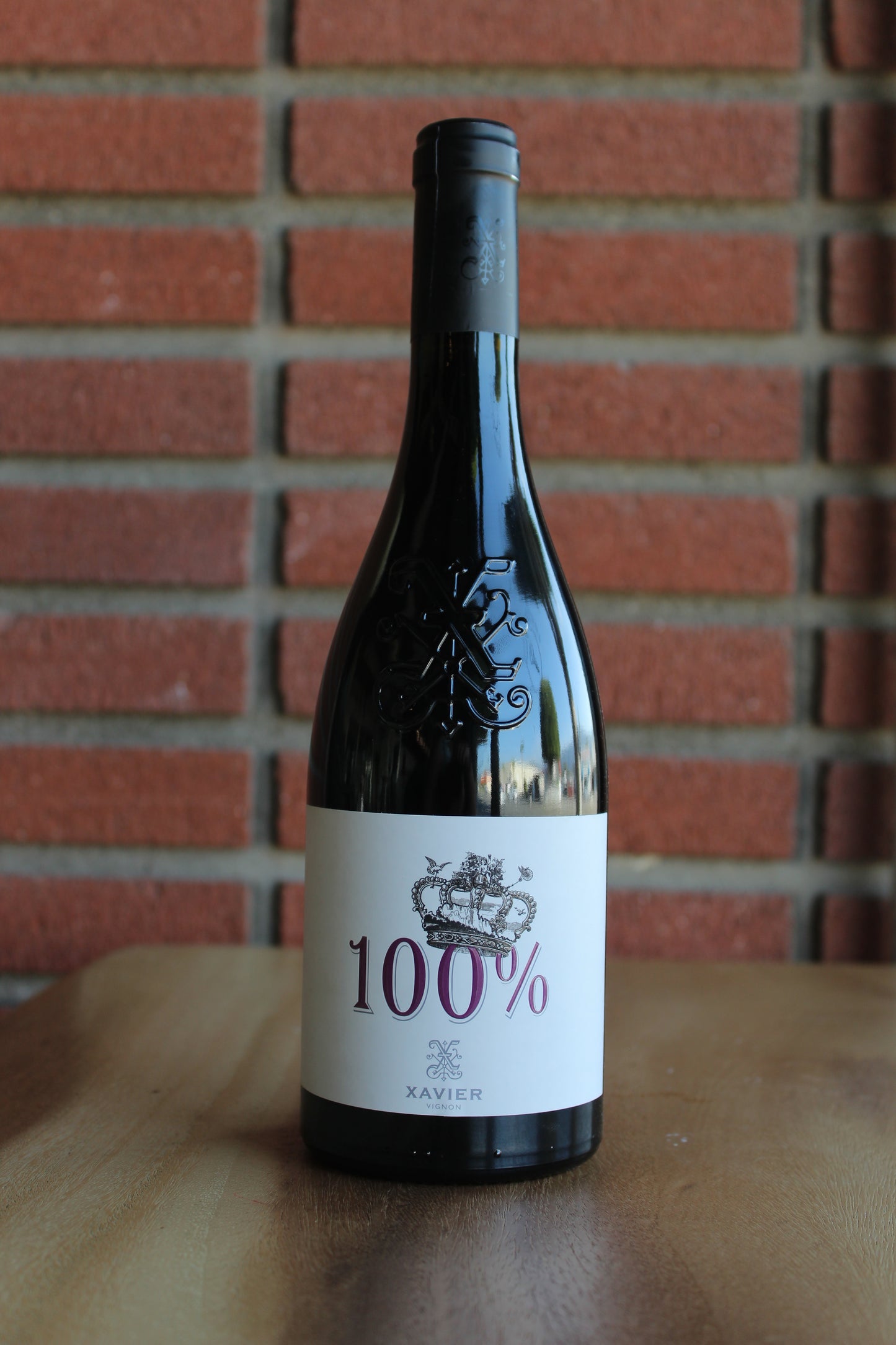 bottle of xavier vignon 100 cotes du rhone 2019 on wood table with a red brick background