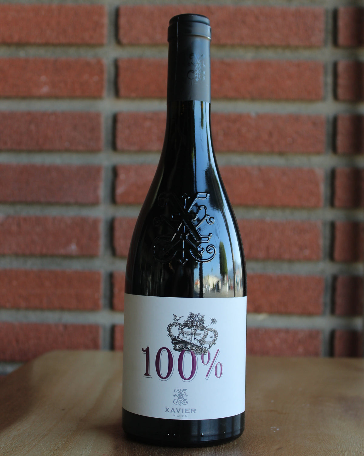 bottle of xavier vignon 100 cotes du rhone 2019 on wood table with a red brick background