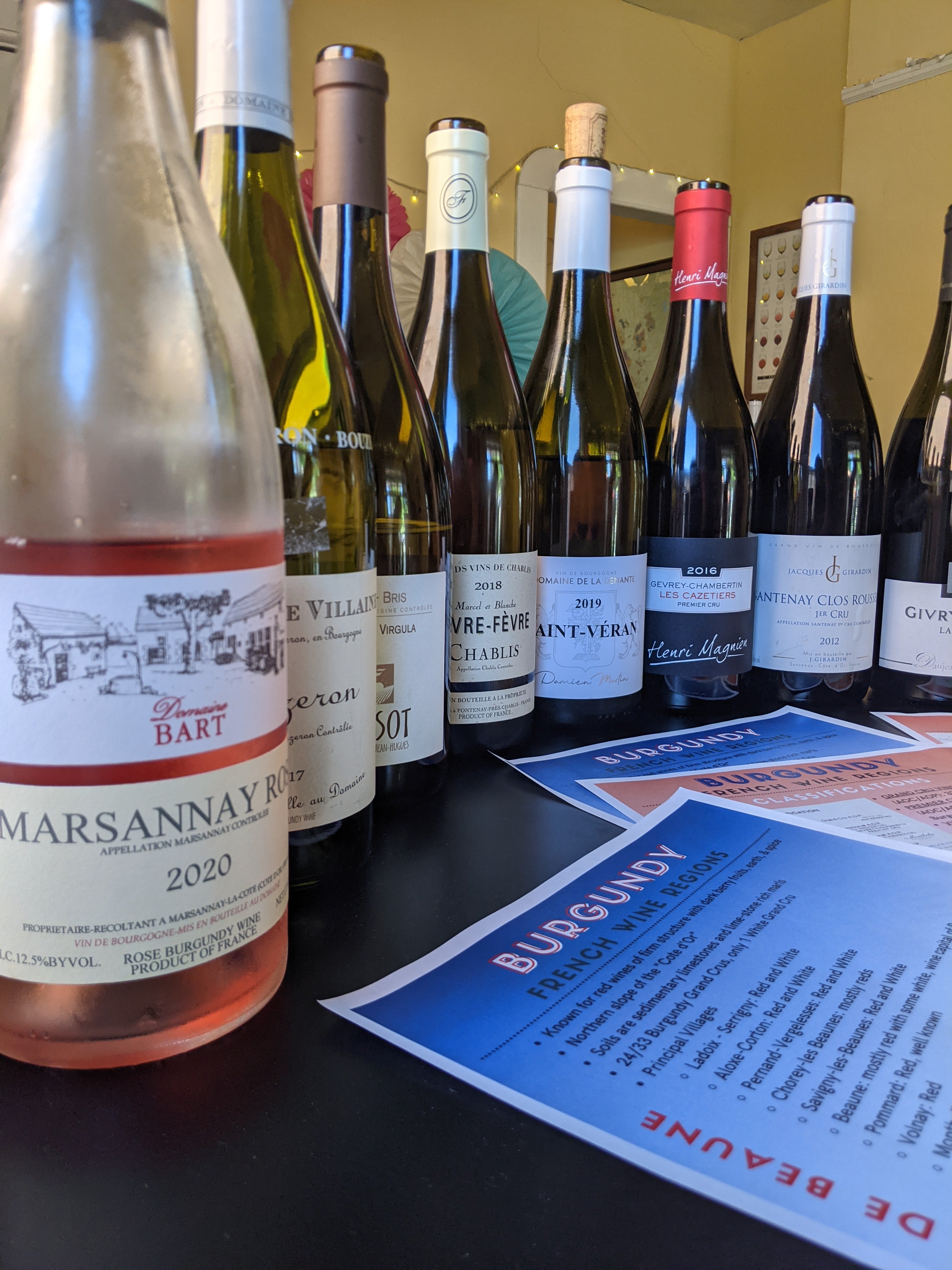 Row of French wine bottles with visible labels on a dark surface, with a Burgundy region sign in the background.