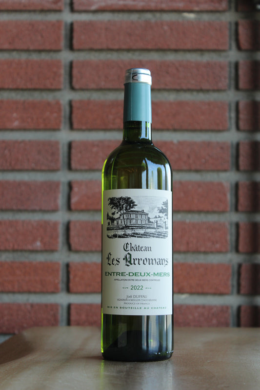 A bottle of Chateau Les Aromans Bordeaux Blanc - Entre Deux Mers white wine stands on a wooden surface against a red brick wall background.