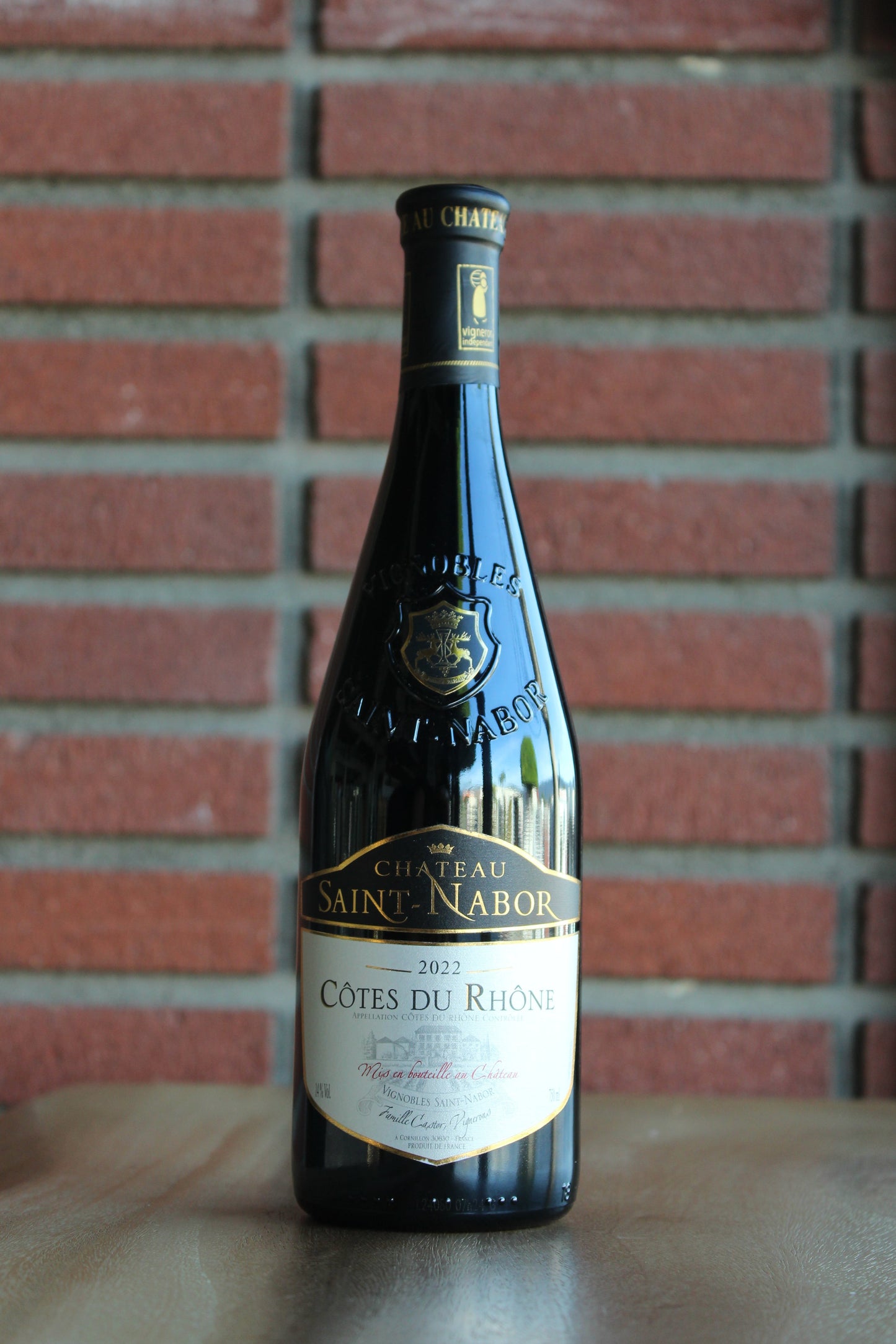 Bottle of Chateau Saint Nabor Cotes du Rhone Red Blend 2022 wine on a wood surface against a brick background