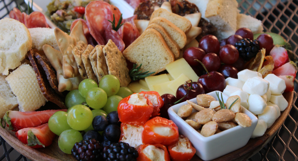Assorted charcuterie board with bread, cheese, fruits, and nuts on a wooden board.