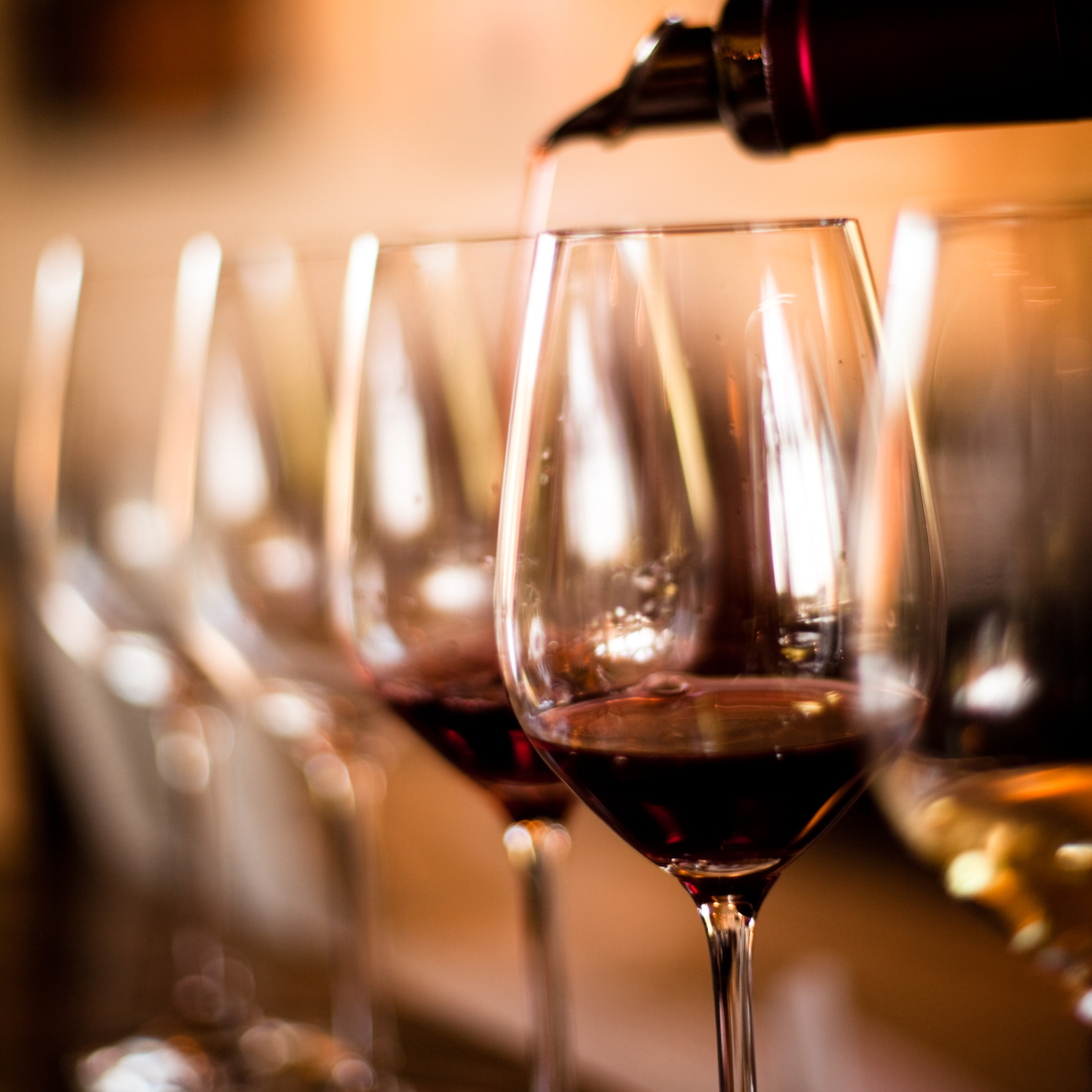 close up of wine glasses filled with different colors of wine, a wine is being poured into one out of focus