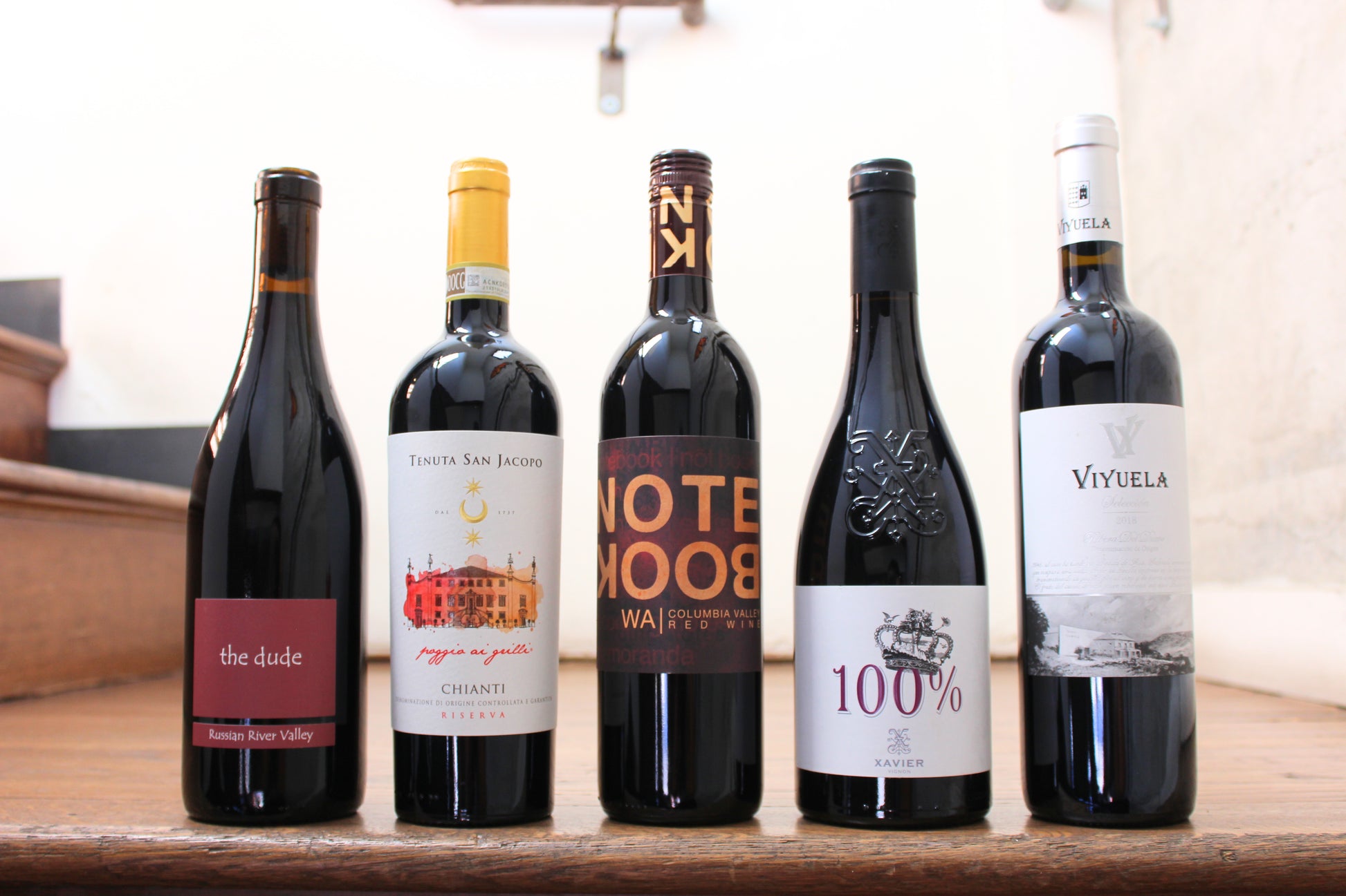 Five wine bottles with various labels on a wooden surface