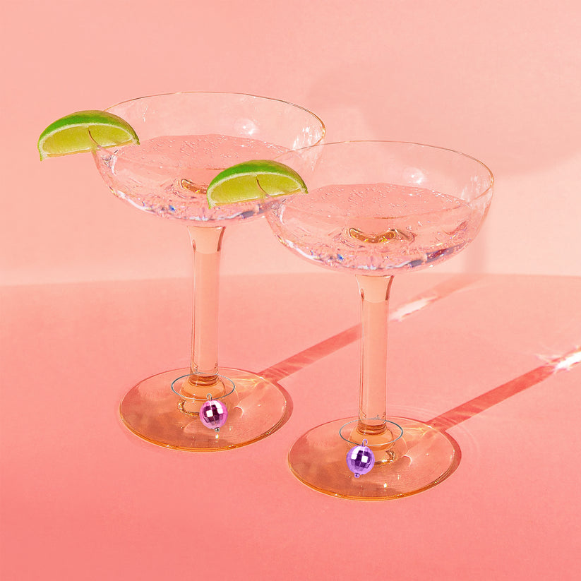 two coupe glasses with clear liqueid and disco ball drink charms