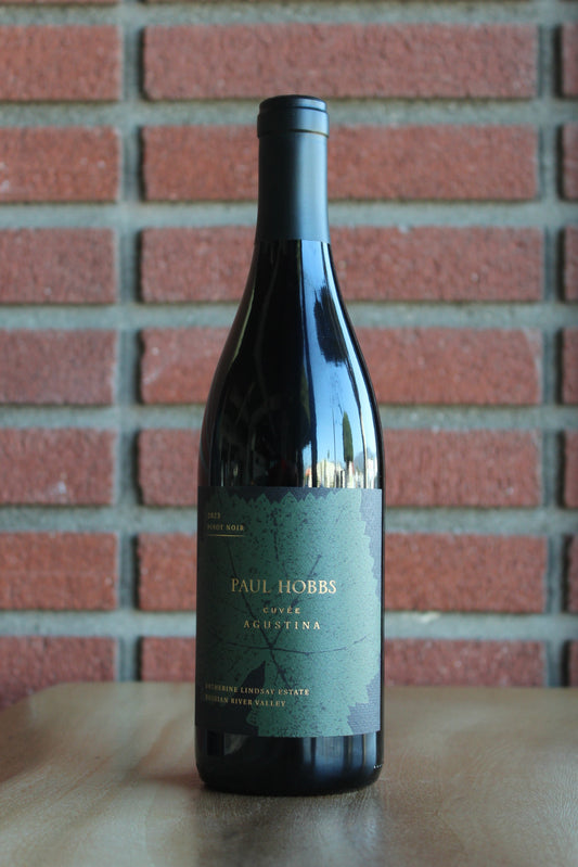 Bottle of Paul Hobbs 2023 Cuvee Agustina Pinot Noir 100 point wine - Wine bottle with a label on a wooden surface in front of a brick wall
