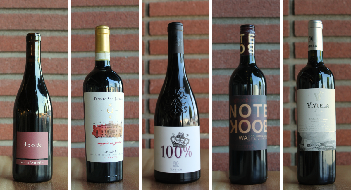 Five wine bottles with labels displayed against a brick wall.