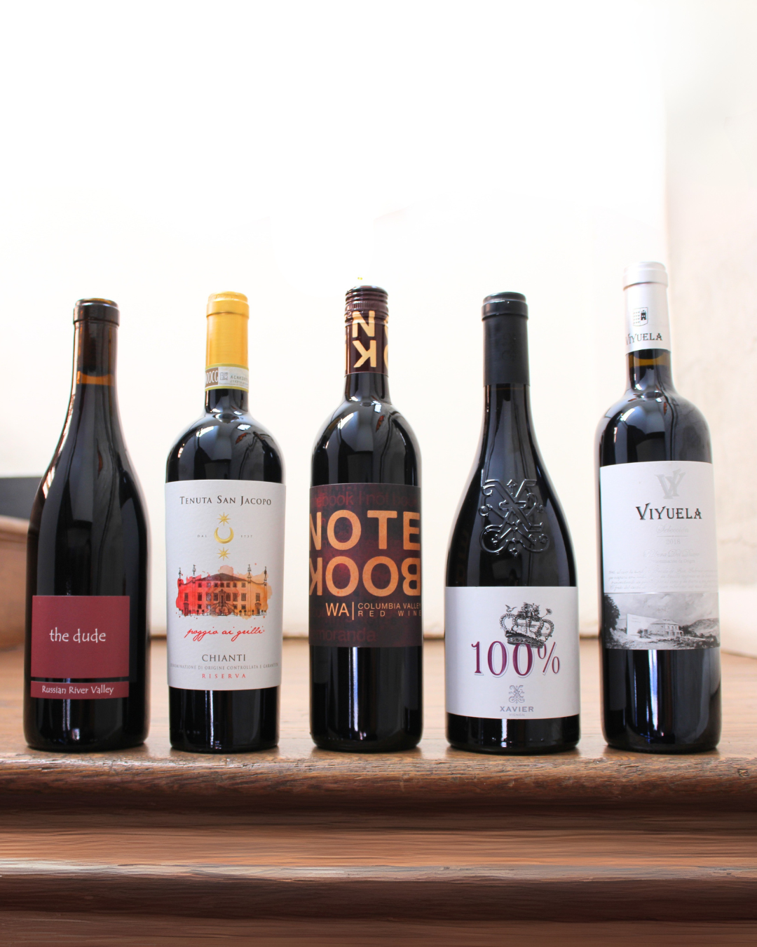 Five wine bottles with various labels on a wooden surface