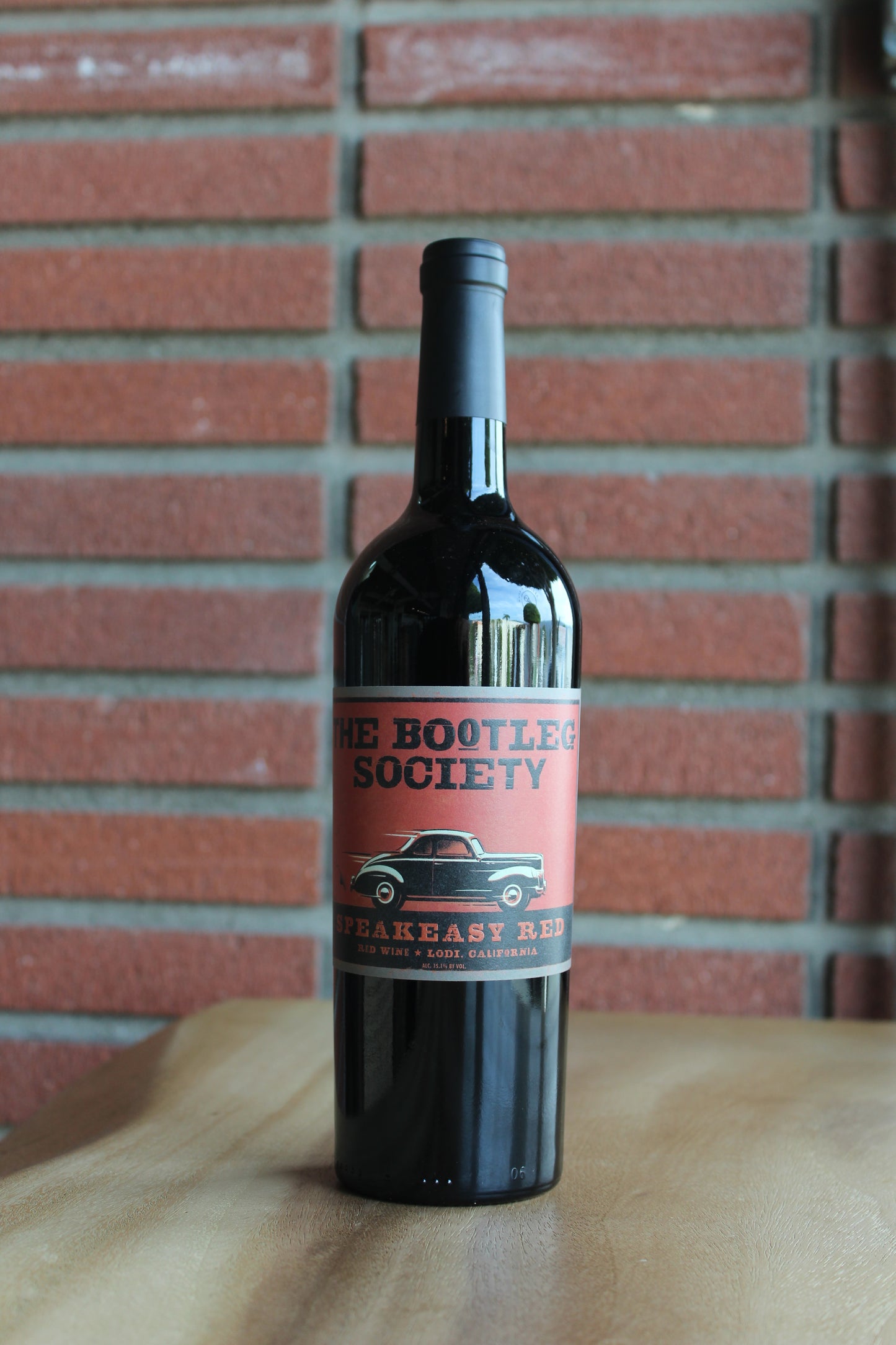 Bottle of St. Amant Bootleg Speakeasy Red Blend 2022 from Lodi, CA, on a rustic wood surface with a red brick background.