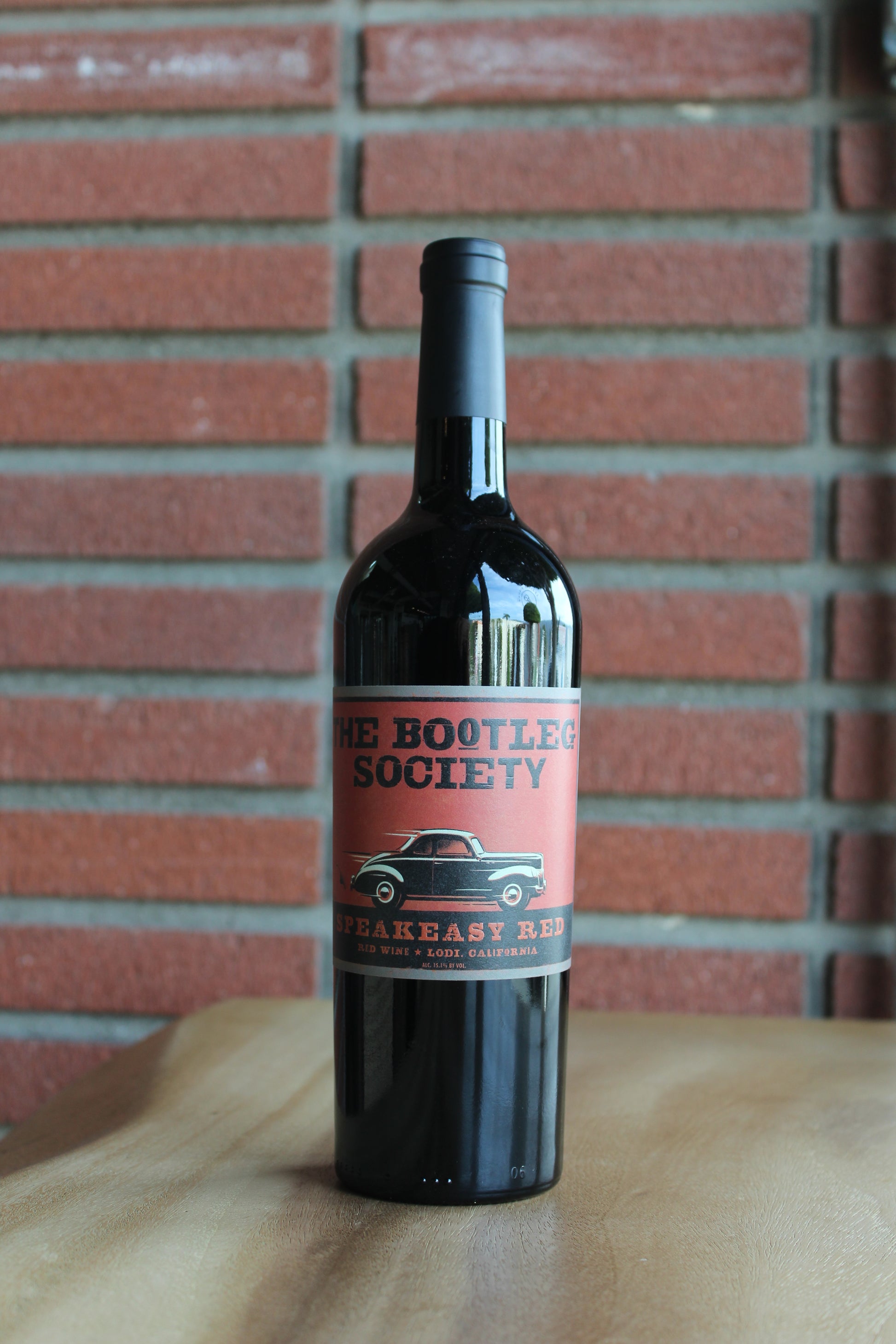 Bottle of St. Amant Bootleg Speakeasy Red Blend 2022 from Lodi, CA, on a rustic wood surface with a red brick background.