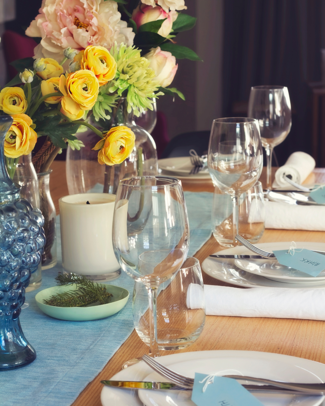 Elegant table setting with flowers, glasses, and cutlery on a wooden table.