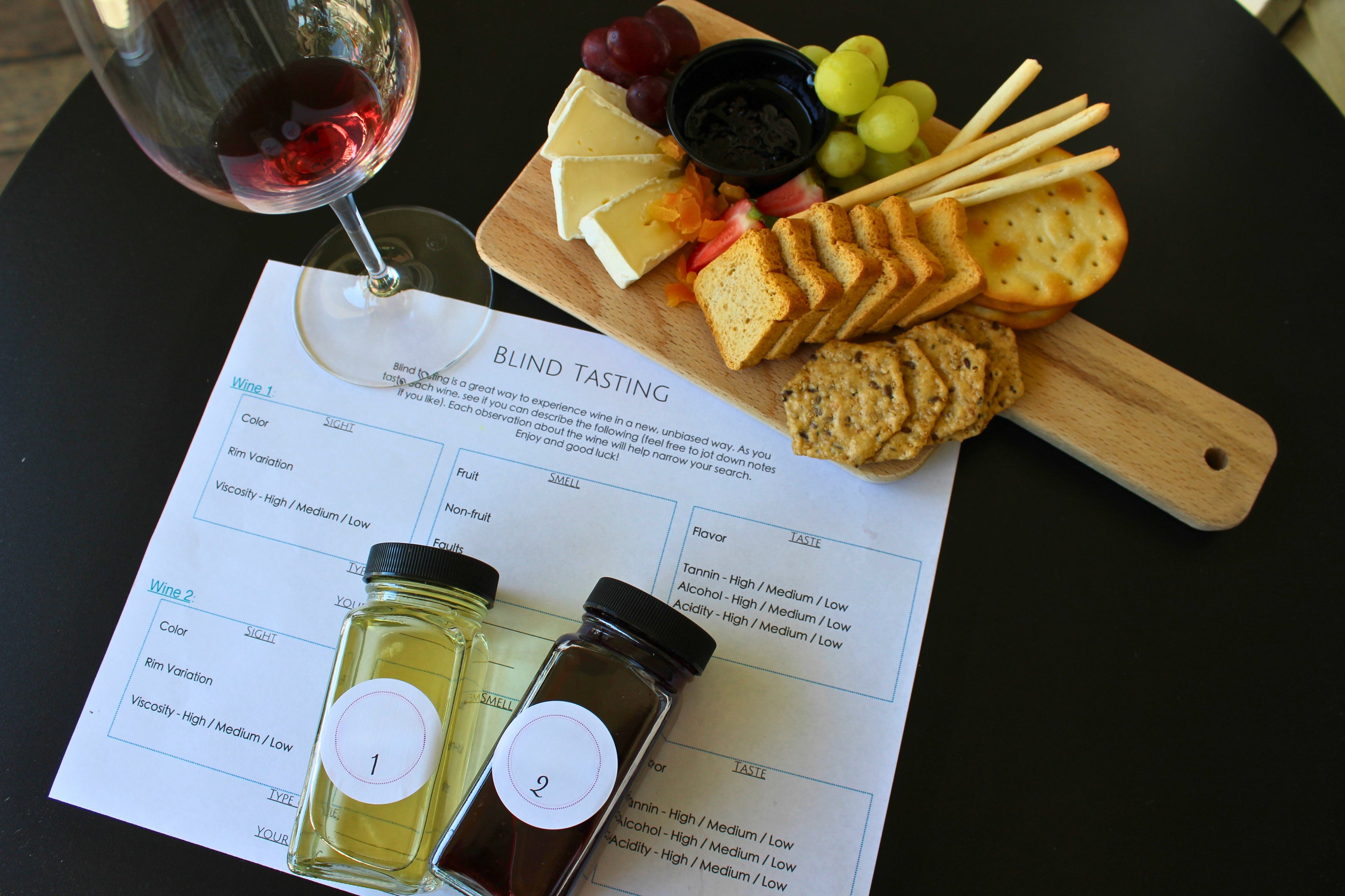 Wine tasting setup with a glass of red wine, cheeseboard, crackers, and two bottles on a menu.