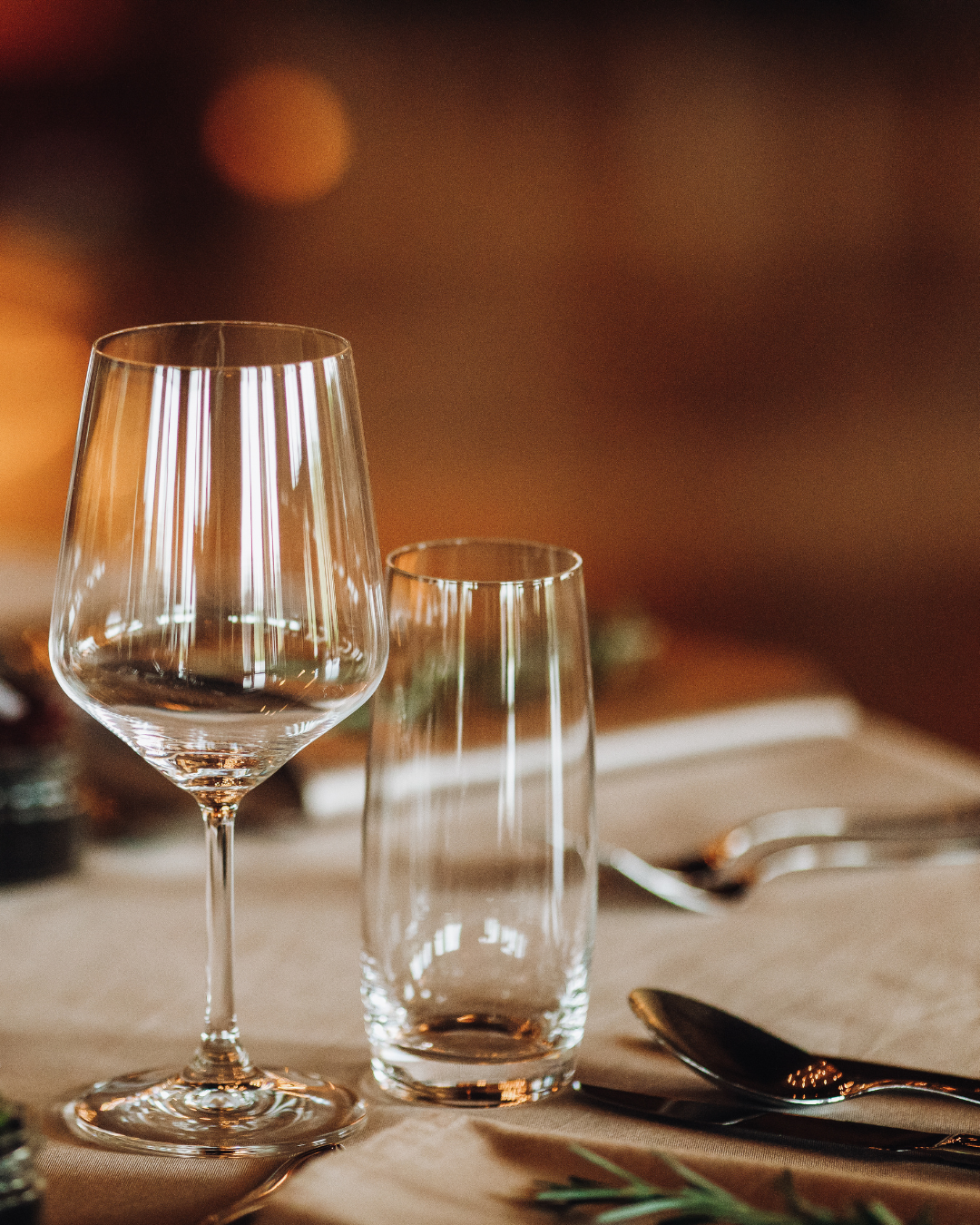 Two clear glasses on a table with a warm, blurred background
